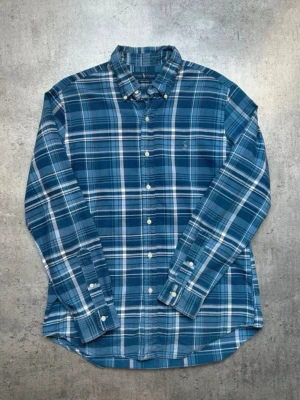 Blå rutig skjorta från Polo Ralph Lauren - Klassisk blå och vit rutig skjorta från Polo Ralph Lauren med lång ärm och knappar framtill. Skjortan har button-down krage och diskret broderad logga på bröstet. Perfekt för en avslappnad men ändå stilren look.
