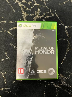 Medal of Honor till Xbox 360 - Medal of Honor till Xbox 360 är ett actionfyllt FPS-spel utvecklat av DICE och EA. Omslaget är grått och svart med en soldat i fokus. Spelet har multiplayerläge och är PEGI 18-märkt. Kommer i klassiskt grönt Xbox 360-fodral av plast.