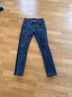 Grå slim fit jeans från nudie  - Säljer ett par grå slim fit jeans från nudie med klassisk femficksdesign och dragkedjegylf. Jeansen har raka ben och är tillverkade i ett mjukt denimtyg som sitter snyggt. Perfekta för dig som gillar en enkel och stilren look.