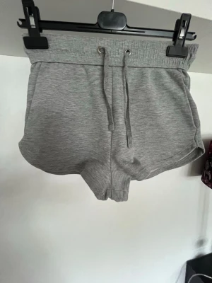 Grå mjuka shorts med dragsko - Säljer ett par grå mjuka shorts med bred resår i midjan och dragsko framtill. Shortsen har en sportig look med rundade kanter och är tillverkade i ett stretchigt, bekvämt material. Perfekta för chill dagar eller träning.💕