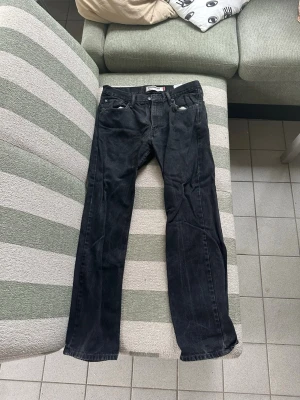 Svarta raka jeans från Levi's - Säljer ett par svarta jeans från Levi's med rak passform och klassisk femficksdesign. Jeansen har bälteshällor och knappgylf. Tillverkade i slitstark denim som passar perfekt till en avslappnad stil. 34x32