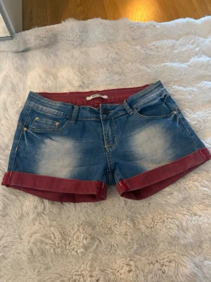 Blå jeansshorts med röda detaljer - Säljer ett par blå jeansshorts från new play i storlek S! De är lågmidjade och ganska korta, super snygga❤️