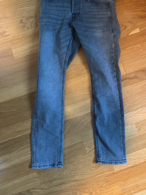 Grå slim fit jeans från Jack & Jones - Snygga grå slim fit jeans från Jack & Jones, modell Glenn. Jeansen har klassisk femficksdesign, normal midja och smal passform hela vägen ner. Tillverkade i stretchigt denim för extra komfort och rörelsefrihet.
