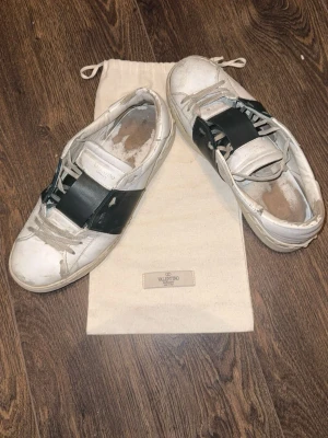 Valentino vita sneakers med svart band - Säljer ett par vita sneakers från Valentino har använt dem en del som man kan se. Sömmen har lossat fram på båda. Och lite på sidan på vänster dojjan men går säkert att fixa.                            Priset går att diskuteras! Hör av er vid frågor