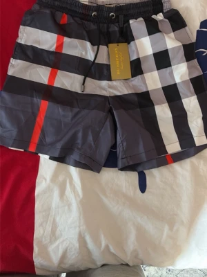 Rutiga badbyxor från Burberry - Snygga badbyxor från Burberry med klassiskt rutmönster i svart, vitt, grått och röda detaljer. De har resårmidja med snörning och innerbyxa i mesh för extra komfort. Perfekta för stranden eller poolen.