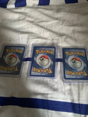 Pokémonkort Cubone 3-pack - Tre samlarkort med Cubone från Pokémon, alla i olika versioner och artwork. Korten har klassisk blå baksida med Pokéball och är skyddade i plastfickor. Perfekt för dig som vill utöka din Pokémonkort-samling med Cubone!