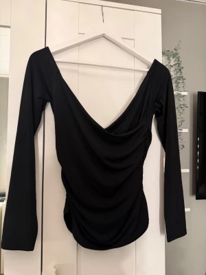 Svart långärmad topp från BikBok - Svart långärmad topp från BikBok med snygg draperad v-ringning och figurnära passform. Helt ny med prislapp kvar, köpt för 300kr. Tillverkad i mjukt syntetmaterial som ger en skön känsla. Perfekt för dig som vill ha en stilren och trendig look.