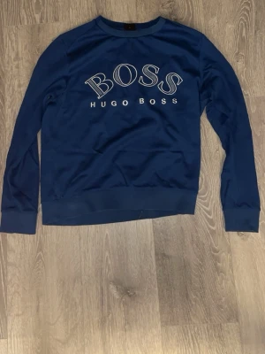 Blå sweatshirt från Hugo Boss - Snygg blå sweatshirt från Hugo Boss med stort BOSS-tryck på bröstet. Tröjan har rund halsringning och långa ärmar, perfekt för en avslappnad och stilren look.