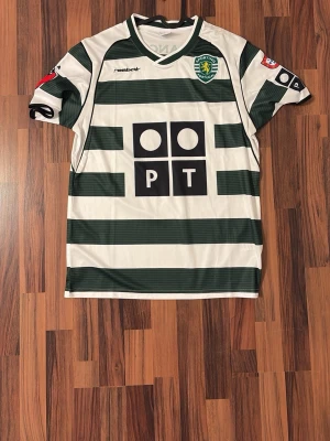Sporting Lissabon 2001 Ronaldo Retro - Sporting Lissabon fotbollströja från Reebok med gröna och vita breda ränder. Tryck på bröstet och ryggen med nummer 28 och namn. Korta ärmar och klassisk sportig passform. Perfekt för fotbollsfans!