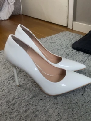 Vita lackade klackskor med spetsig tå - Säljer ett par klassiska vita pumps i lackat material med spetsig tå och hög klack. Skorna har en stilren design och en elegant siluett som passar till många olika outfits. Innersulan är beige och klacken är smal.(Svart fläckarna på skorna är Franslim och jag torkar av dem innan jag skickar dem, dem har alltså inga prermanenta fläckar). 