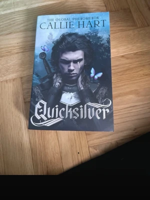 Quicksilver av Callie Hart - Säljer boken 'Quicksilver' av Callie Hart. Omslaget är blått och svart med fantasytema, svärd och fjärilar. Perfekt för dig som gillar äventyr, magi och romantik i en spännande värld. Mjukpärm och engelskt språk.