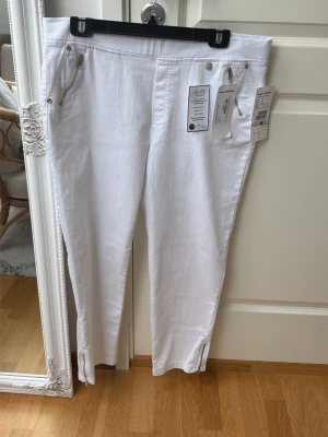 Vita kortare jeans från Anna Montana (strl 44) - Säljer ett par vita lite kortare jeans från Anna Montana med superstretch, perfect fit och body shape med dragkedjedetaljer framtill. Byxorna har må slitsar vid bensluten. Perfekta för dig som gillar stilrena och bekväma jeans.