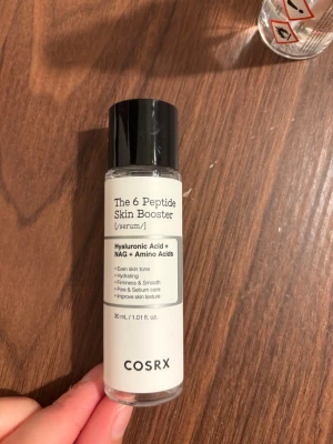 COSRX The 6 Peptide Skin Booster - Oöppnad COSRX The 6 Peptide Skin Booster är ett genomskinligt serum i en cylinderformad plastflaska med svart lock. Innehåller hyaluronsyra, NAG och aminosyror för återfuktning, jämn hudton och förbättrad hudstruktur. Volymen är 30 ml.