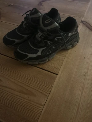 Svarta och grå Asics sneakers - Snygga sneakers från Asics i svart och grått med meshpaneler och detaljer i syntetmaterial. Skorna har klassisk snörning och en robust sula som ger bra stöd. Perfekta för dig som gillar sportig stil och vill ha bekväma skor till vardags.