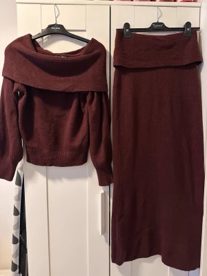 Vinrött stickat set med off shoulder - Säljer ett vinrött stickat set med off shoulder-tröja och matchande lång kjol. Tröjan har bred krage och långa ärmar med ribbade muddar. Kjolen är rak och lång med samma stickade material. Perfekt för dig som gillar mysiga och trendiga set.