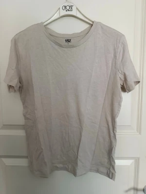 Beige basic t-shirt från 157 - En enkel beige t-shirt från 157 med rund hals och korta ärmar. Tillverkad i mjukt bomullsmaterial och har en klassisk passform som funkar till det mesta. Perfekt för dig som gillar minimalistisk stil.