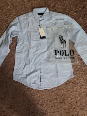 Ljusblå skjorta från Polo Ralph Lauren - En gång använd!!!🚨 Klassisk ljusblå skjorta från Polo Ralph Lauren med lång ärm och button-down krage. Skjortan har en stilren design med knappar framtill och diskret logga på insidan. Tillverkad i mjukt bomullstyg och levereras med originalpåse.