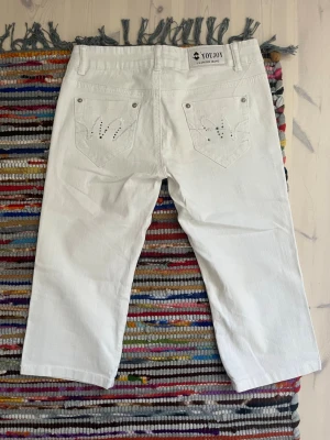 Lågmidjade capris  - Jättesnygga vita trekvartsbyxor/capris! Väldigt bra skick och coola detaljer. Midjemått rakt över: 34,5 cm innerbenslängd: 43 cm