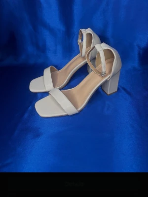 Beige sandaler med blockklack - Jättefina stilrena beige sandaler med bred rem över tårna och justerbart ankelband med spänne. Köpt på Tradera men tyvärr för små. Aldrig använda, endast provade av mig. Skorna har fyrkantig tå och stabil blockklack. Tillverkade i ett slätt syntetmaterial som känns bekvämt på foten.