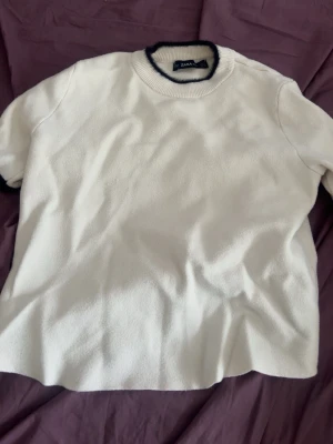 Vit stickad topp från Zara - Vit stickad topp från Zara med korta ärmar och rund halsringning. Svart kant runt halsen och ärmsluten ger en snygg kontrast. Perfekt för dig som gillar enkel och stilren design. Storlek S, helt nytt skick aldrig använd. Priset går att diskutera. 