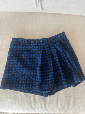 Blåsvarta skorts med rutigt mönster  - Snygga skorts i blått och svart med klassiskt hundtandsmönster. Skorts-modellen ger en kjol-look framifrån men är shorts baktill. Materialet känns mjukt och lite tjockare. Inga synliga fickor eller dragkedjor.