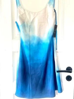 Blå och vit kortklänning med draperad rygg - Säljer en snygg kortklänning från NA-KD med gradient i blått och vitt. Klänningen har smala axelband och en draperad öppen rygg som ger en cool look. Perfekt för sommarens alla tillfällen. Materialet känns lätt och luftigt.