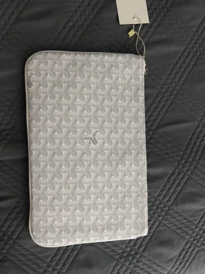 Handväska herr - Snygg handväska för men i gråvitt med geometriskt mönster och dragkedja. Fodralet har en stilren look och är perfekt för att skydda din dator eller surfplatta. Materialet känns tåligt och har en mjuk finish. Passar dig som gillar minimalistisk och modern design.