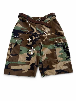 Camouflage cargo shorts med nitar - Customized by jutsol. Säljer ett par camouflagefärgade cargo shorts med coola nitar och dekorativa detaljer. Shortsen har flera fickor och ett brunt bälte i midjan. Perfekta för dig som gillar streetwear och vill sticka ut.