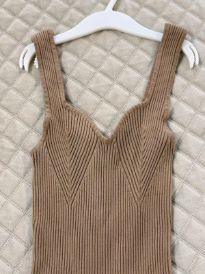 Beige ribbad stickad klänning - Snygg beige ribbad klänning med breda axelband och v-ringad urringning. Klänningen är figurnära och har ett stilrent, minimalistiskt uttryck. Perfekt för dig som gillar en enkel men trendig look.