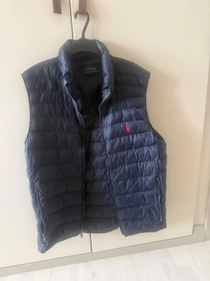 Mörkblå dunväst från Polo Ralph Lauren - Snygg mörkblå dunväst från Polo Ralph Lauren med quiltad design och dragkedja framtill. Ny pris 3200