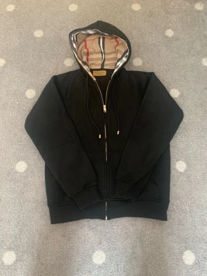 Burberry hoodie zip-up svart - Burberry Hoodie Fleece Zip-Up – Svart  Säljer en svart Burberry hoodie med dragkedja i mycket fint skick. Tröjan är väldigt tjock och varm, perfekt för kallare dagar. Insidan har ett extremt mjukt, ullaktigt fleecefoder som känns väldigt skönt mot huden och gör hoodien riktigt bekväm att bära.  Storleken är märkt XL, men den upplevs mindre i passformen och passar bäst för personer som är ungefär 170–175 cm långa beroende på önskad passform.  💰 Pris: 1200 kr ⚡ Vid snabb affär: 999 kr  