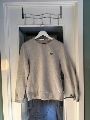 Grå sweatshirt från Lee - En stilren grå sweatshirt från Lee med rund halsringning och diskret logotyp på bröstet. Tröjan har långa ärmar och ribbade muddar vid ärmslut och nederkant. Perfekt för en avslappnad och trendig look.