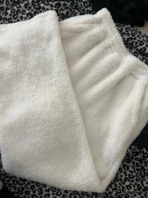 Vita fluffiga loungewear-byxor - Mysiga loungewear-byxor i vitt, supermjukt och fluffigt material som känns som fleece. Byxorna har resår i midjan och en avslappnad passform, perfekta för hemmamys eller lata dagar. Inga synliga fickor eller detaljer. Märke och storlek ej angivet.