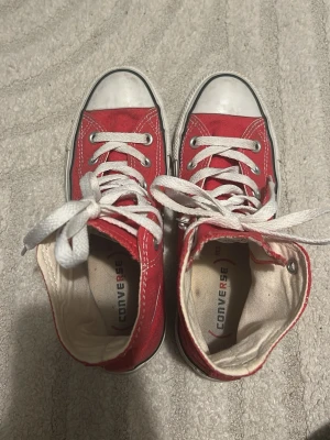 Röda Converse All Star Highs - Klassiska röda Converse All Star high top sneakers med vit gummisula och tå, vita skosnören och ikonisk logga på sidan. Skorna är i canvasmaterial och har metallöljetter för snörningen. Perfekta för en avslappnad och cool stil. Använt bara en gång, jätte bra skick!