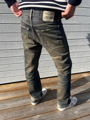 Levis 504 - Säljer ett par klassiska blå Levi's jeans med raka ben och tydliga slitningar. Jeansen har fem fickor, synliga sömmar och en vintage tvättad look. Tillverkade i bomull och har den ikoniska Levi's-lappen bak i midjan.