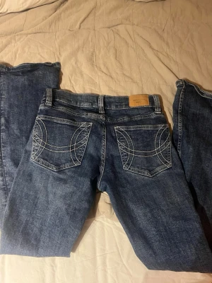 Blå lågmidjade jeans från Perfect Jeans Gina Tricot  - Säljer ett par blå lågmidjade jeans från Perfect Jeans i storlek 36. Jeansen har utsvängda ben och coola bakfickor med vit kontrastsöm i ett unikt mönster. Klassisk femficksmodell och tillverkade i slitstark denim. Perfekta till din vardagsstil!