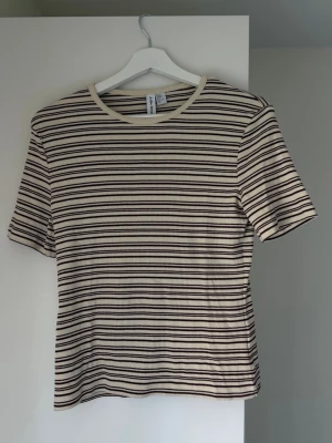 Randig ribbad t-shirt från & other stories  - Snygg ribbad t-shirt från & other stories med beige och bruna horisontella ränder. T-shirten har korta ärmar och rund halsringning. Perfekt för dig som gillar en enkel men trendig stil.