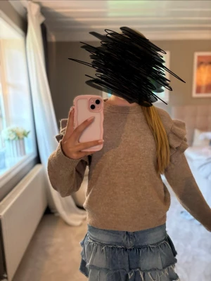 Beige stickad tröja med volangärmar från H&M i strl 146/152 - Supersöt beige stickad tröja med långa ärmar och volangdetaljer på axlarna. Tröjan har rund halsringning och ribbade muddar vid ärmslut och nederkant. Perfekt för dig som vill ha något gulligt och trendigt i garderoben.