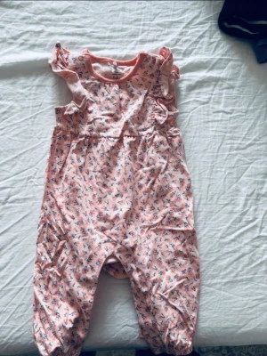 Rosa blommig byxdress Polarn O. Pyret - Söt rosa byxdress från Polarn O. Pyret i storlek 62, med små blommor i blått och vitt. Byxdressen har volangdetaljer vid axlarna och är tillverkad i mjuk bomull. Perfekt för mysiga dagar och lek.
