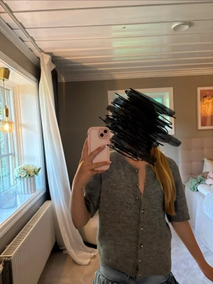 Grå kortärmad kofta från H&M i strl S - Mysig grå kofta från H&M med korta ärmar och rund halsringning. Koftan har knappar framtill i metall och är stickad i ett mjukt material som känns skönt mot huden. Perfekt att slänga över en topp eller bära som den är.