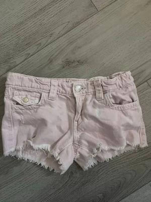 Ljusrosa fransiga jeansshorts - Säljer ett par ljusrosa lågmidjade jeansshorts med fransig kant i storlek 152. Shortsen har blivit missfärgade där bak vid fickan