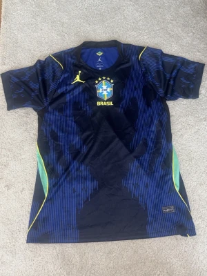Blå Brasilien tränings t-shirt Nike - Snygg blå tränings t-shirt med Brasilien CBF-logga och gula detaljer. Tröjan har korta ärmar, rund hals och coolt mönster i blått och svart. Materialet är lätt och andas, perfekt för fotboll eller gym. Gula och gröna inslag på sidorna. PASSA PÅ NU INFÖR VM!