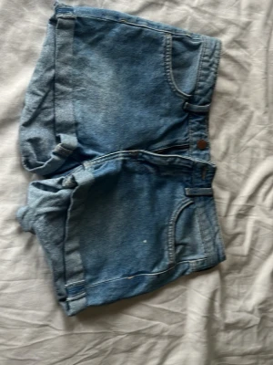 Blå denimshorts med uppvik - Klassiska blå jeansshorts i denim med uppvikta benslut och femficksdesign. De har normal passform och stängs med knapp och dragkedja. Perfekta för varma dagar och enkel att matcha med olika toppar. Använt nån gång 