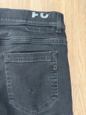 Svarta  jeans från Dondup - Säljer ett par svarta skinny jeans från Dondup med klassisk femficksdesign och diskret logga på bakfickan.. Tillverkade i stretchigt denimtyg för extra komfort. Och jeansen har väldigt feta slitningar! Prutmått finns vid snabb affär!!