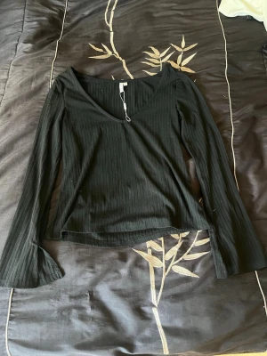 Svart ribbad långärmad tröja  - Snygg svart ribbad tröja med v-ringning och långa ärmar. Modellen har lätt utsvängda ärmslut och är tillverkad i ett mjukt material som sitter bekvämt. Perfekt att styla med jeans eller kjol för en trendig look. Den är helt ny har bara provats.