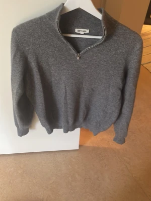 Grå halvzip stickad tröja Soft Goat - Mysig grå stickad tröja från Soft Goat med halv dragkedja och hög krage. Tröjan har långa ärmar och ribbade muddar vid ärmslut och nederkant. Perfekt för lager på lager och enkel att matcha med olika outfits.