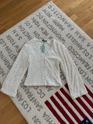 Vit paljettopp med v-ringning - Superfin vit topp från Gina Tricot med v-ringning och långa ärmar. Hela toppen är täckt av glittrande paljetter som ger en riktigt snygg look. Modellen är croppad och har en lätt figurnära passform. Perfekt för dig som vill sticka ut lite extra.