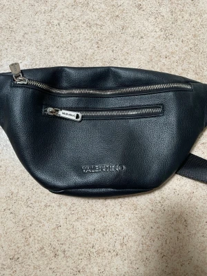 Svart shoppingväska från Valentino - Snygg svart shoppingväska från Valentino i slätt konstläder. Väskan har två dragkedjefack framtill och justerbar axelrem i textil. Perfekt för dig som vill ha en stilren och praktisk accessoar med plats för det viktigaste. Diskret Valentino-logga framtill.pris går att diskutera för fler frågor skriv gärna 🙏😊