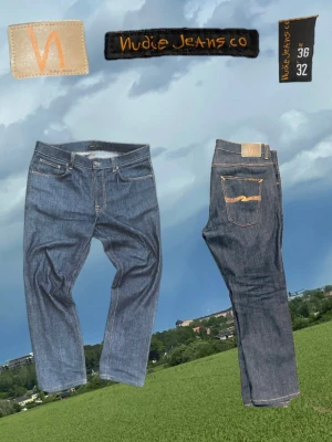 Blå jeans från Nudie Jeans Co - Säljer ett par klassiska blå jeans från Nudie Jeans Co med raka ben och orangea sömmar. Jeansen har fem fickor och en snygg logga på bakfickan. Tillverkade i slitstarkt denimtyg, perfekta för en avslappnad och trendig look.