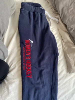Mörkblå Women's Hockey mjukisbyxor - Mörkblå mjukisbyxor med röd brodyr 'WOMEN'S HOCKEY' och vit siluett av hockeyspelare på benet. Byxorna har resår i midjan med vit dragsko och är perfekta för chill dagar. Märket är Wear by Maria Rooth, etablerat 2006. Pruta om så behövs för jag vill bara bli av med de🥰